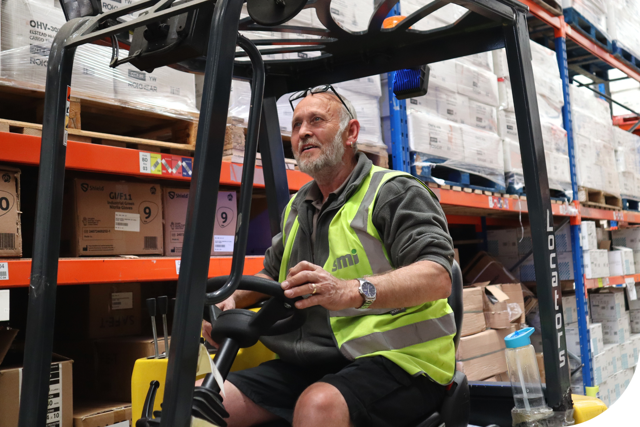 Man in hi-vis driving a forklift inside a warehouse.